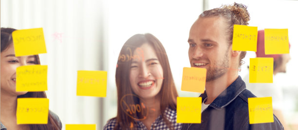 时髦迷人的年轻白人男子和年轻的亚洲中国女孩讨论和头脑风暴一起在玻璃墙分享商业想法项目计划与贴它的便利贴。营销计划的概念。图片下载