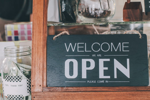 透过咖啡店门上的玻璃窗打开招牌特写。景深浅。咖啡馆/餐厅的橱窗上有一个商业招牌，上面写着“请进，我们还在营业”。图像抽象模糊餐厅与人。餐厅与客户图片下载