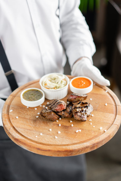 侍者端着一个盘子，上面放着烤好的肝脏。在木板上工作烧烤餐厅的菜单，一系列不同肉类的照片。酸菜和两种酱汁图片下载