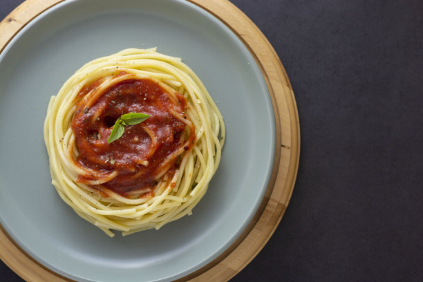 加蕃茄酱和罗勒的意大利面，放在盘子里，背景颜色较深。意大利面板隔离。顶部视图与复制空间。图片下载