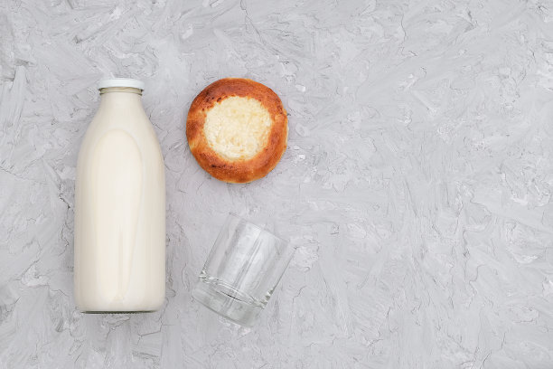 牛奶在玻璃瓶，一个空的杯子和新鲜烤面包在灰色的背景与复制空间。平放俯视图图片下载