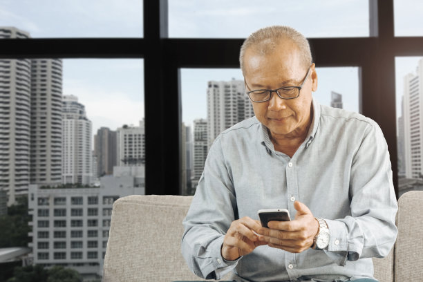 夏天，年长的男人独自呆在家里的室内，现在他正坐在沙发上玩手机图片下载