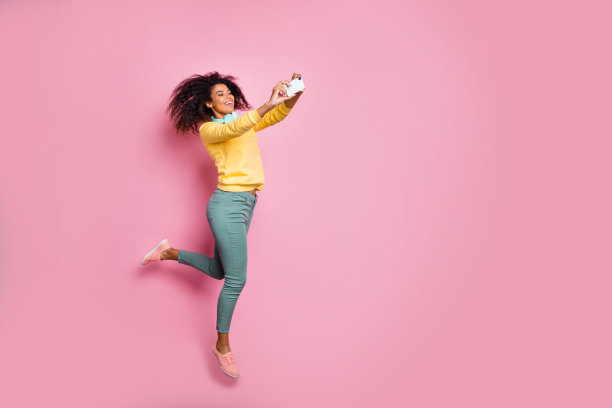 旅行运动生活方式使人们现代科技的概念。全照片欢快，无忧无虑，兴奋的时尚风格的女孩，使自画像跳穿黄色运动衫长裤孤立的粉色背景图片下载