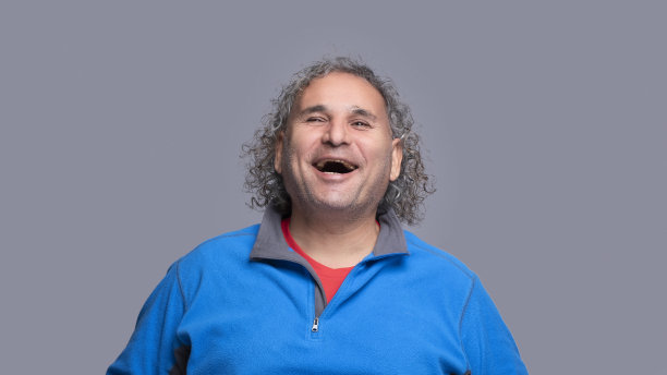 在灰色背景前开怀大笑的卷发男人图片下载