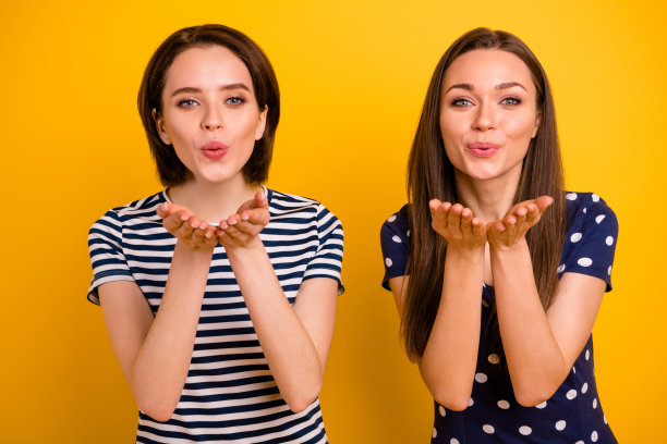 照片中的两个漂亮的女士举起手臂送帅气的男孩空中吻穿夏天休闲时尚t恤孤立的黄色背景图片下载