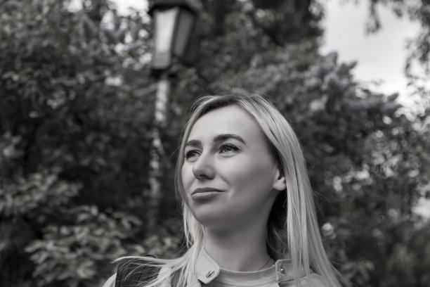 一个金发女孩的黑白肖像在街道上的黑白图像，模糊的背景是公园里的树。图片下载