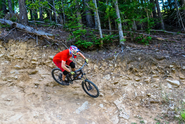 穿着橙色t恤的自行车手在岩石山上骑山地车。图片下载