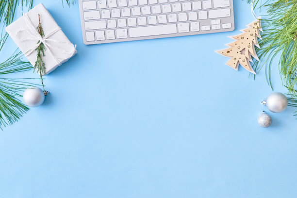 平铺的圣诞家庭办公桌子上有松枝和键盘，蓝色背景上有圣诞装饰品图片下载
