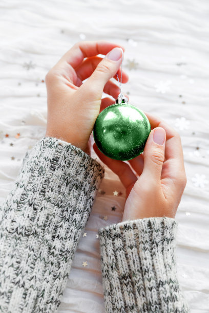 女人手持新年装饰品-闪闪发光的新薄荷彩色球为圣诞树。白色织物背景与银色雪花纸屑。俯视图，平放。图片下载