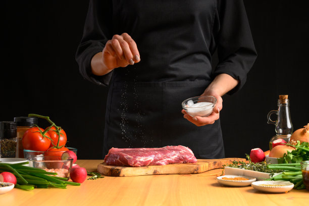 厨师给牛排烤锅加盐。准备新鲜的牛肉或猪肉。深色背景的水平照片。图片下载