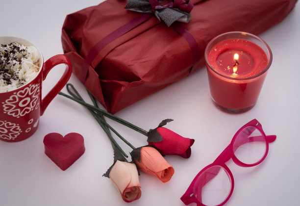 白色的桌子与红色的配件，礼品，蜡烛和鲜花。一杯加奶油的咖啡图片下载