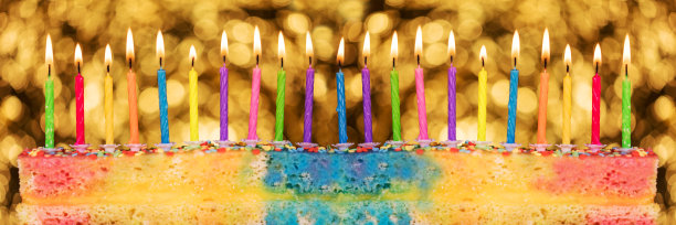 五彩缤纷的蜡烛放在五彩缤纷的蛋糕上，在金色闪闪发光的背景前图片下载