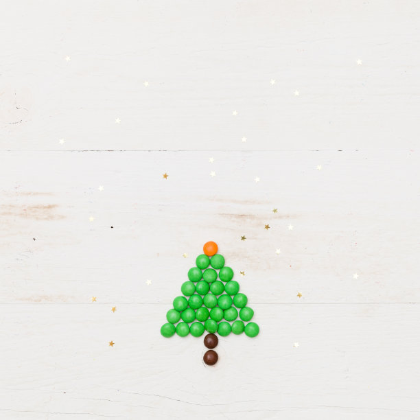 顶视图上的一个有趣的圣诞树糖果与小金色星星五彩纸屑在白色的木制背景。冬天，圣诞节和新年快乐的概念图片下载