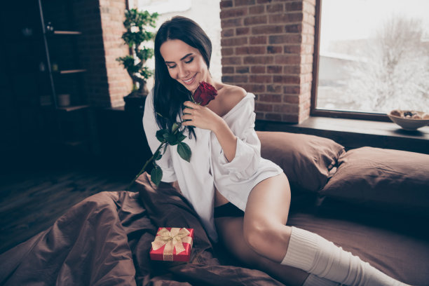 漂亮的女士坐在床上的照片与小礼品盒和新鲜的红玫瑰惊喜从丈夫穿长袜白衬衫和内裤室内图片下载