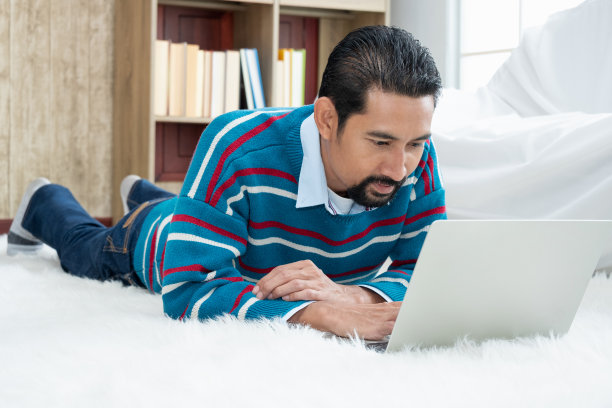 在客厅里，一个成年的商人带着一台笔记本电脑躺在羊毛地毯上，看起来很有尊严和富有。图片下载