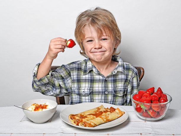 可爱的男孩坐在早餐桌前吃着煎饼和草莓图片下载