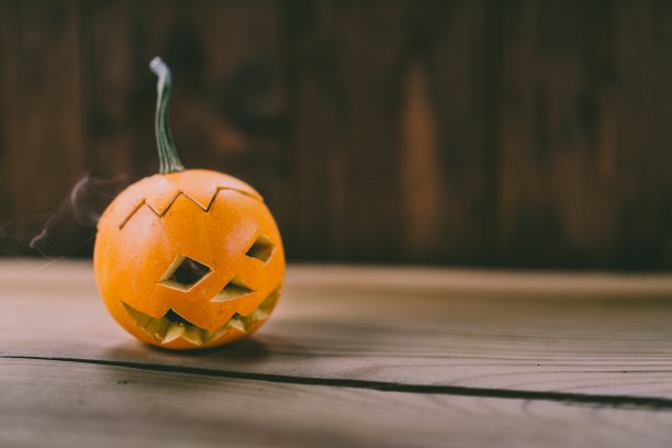 特写照片的小雕刻南瓜在黑暗的木制背景与烟出来的眼睛和嘴图片下载