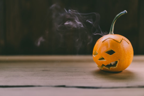 特写照片的小雕刻南瓜在黑暗的木制背景与烟出来的眼睛和嘴图片下载