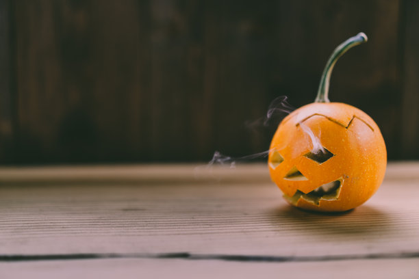 特写照片的小雕刻南瓜在黑暗的木制背景与烟出来的眼睛和嘴图片下载