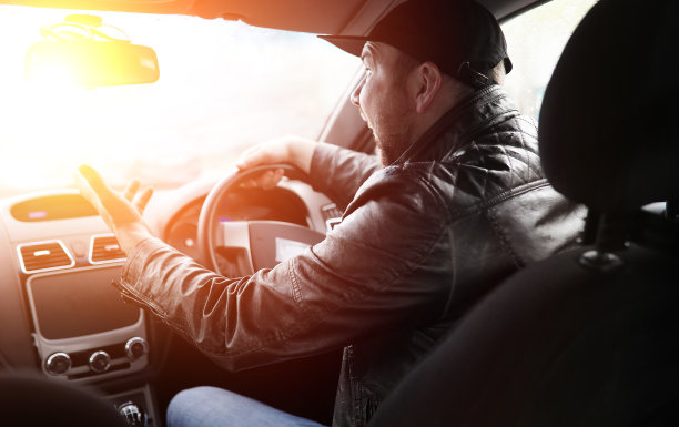 一个男人开车。司机正开着汽车沿路行驶。太阳使开车的人看不见。图片下载