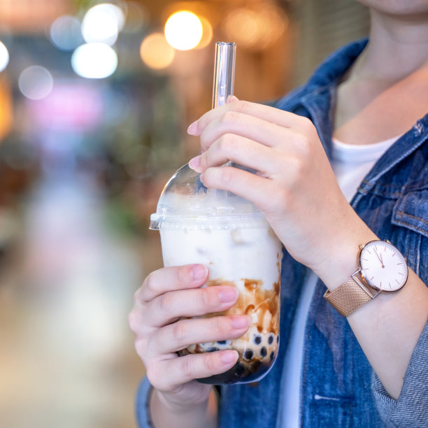 台湾夜市，一名年轻女子拿着玻璃吸管喝着红糖口味的珍珠奶茶图片下载