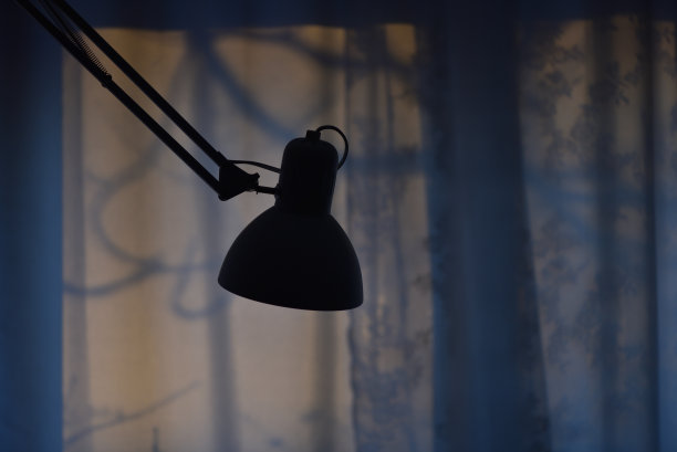 一盏台灯的剪影在一扇窗户的背景上，在早上的黎明，工作到早上，晚上工作。图片下载