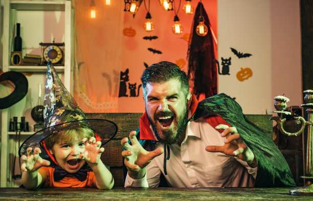 万圣节的家庭聚会。男人和男孩吓唬客人。父亲和儿子在家里玩恐怖的万圣节游戏。有趣的朋友，快乐的童年。图片下载