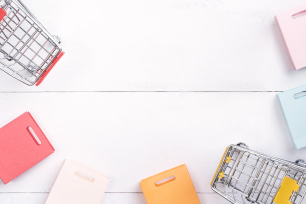 抽象的设计元素，年度销售，购物季节的概念，小手推车与彩色纸袋在白色木制桌子的背景。图片下载