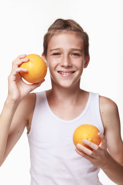 一个穿着白色运动衫的年轻人笑着，帮着他，拿着两个橙子。图片下载