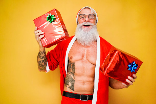 时尚的纹身圣诞老人送圣诞礼盒-快乐的老人与冬季节日服装持有礼物-冬季，趋势，假期概念-关注他的脸图片下载