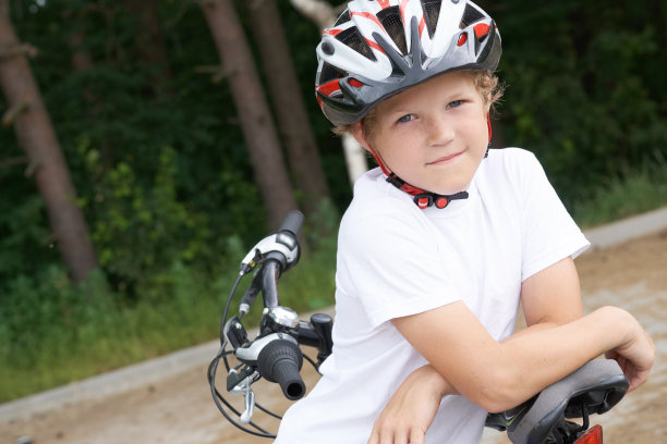 一个戴着保护头盔的小白种男孩靠在自行车上，摆姿势准备拍照。少年准备骑自行车在公园在夏天的一天。周末的活动。图片下载