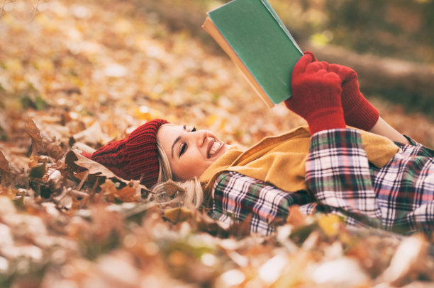 年轻女子躺在秋天的草地上，读着她最喜欢的书图片下载