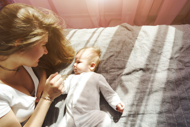 阳光下，母亲抱着刚出生的儿子躺在床上图片下载