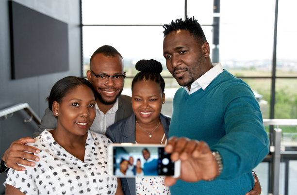 四个快乐，迷人的非洲裔美国同事在明亮的现代办公空间一起用手机自拍图片下载