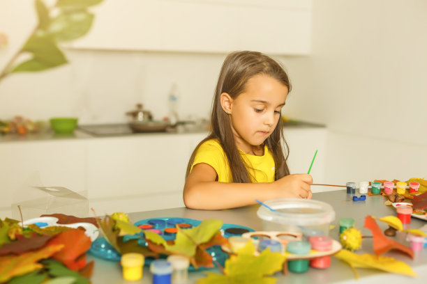 小女孩用水粉在秋天的黄叶上作画，儿童艺术，儿童创意，秋天艺术。图片下载