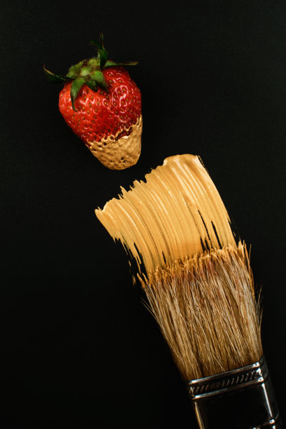 木制的猪鬃刷，金色的油漆和红色的新鲜草莓在黑色的背景。暗键，简约风格。图片下载
