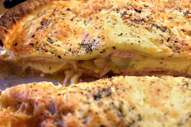 土豆、奶酪、火腿和洋葱派的特写图片，用玉米饼而不是糕点制成，金色融化的奶酪，盛在瓷盘上，切成两半，显示分层的馅图片下载