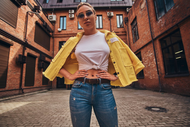 低角度照片的漂亮女人在对称的院子里戴墨镜和牛仔布。图片下载