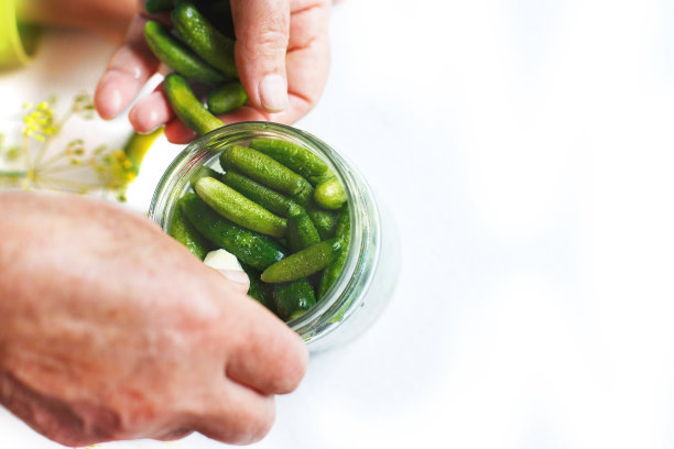 玻璃罐里的腌黄瓜。小黄瓜黄瓜。女人在白色的背景上腌制黄瓜图片下载