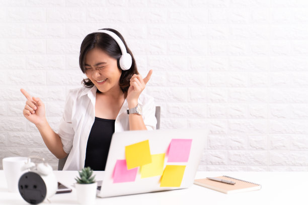 在办公室戴着耳机听音乐的快乐女人图片下载