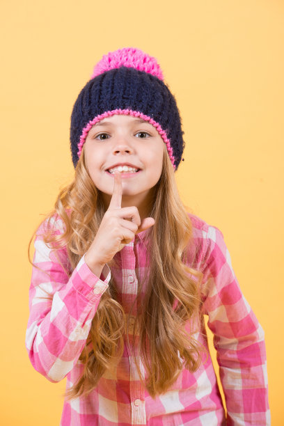 女孩戴着帽子，格子衬衫微笑在橙色的背景图片下载
