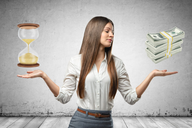 在灰色的墙壁背景上，年轻的女商人手里拿着沙玻璃和一捆捆的美元图片下载