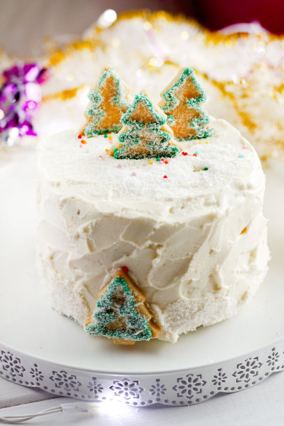 新年圣诞自制的节日蛋糕与白奶油霜装饰绿色的圣诞树饼干花环和灯的背景。蛋糕风格的庆祝活动图片下载