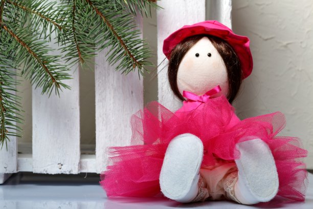 穿着粉红色衣服的自制布娃娃。以一根冷杉树枝和一个白色的木箱为背景。图片下载