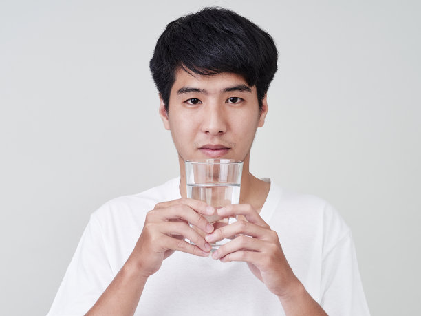 年轻的亚洲男人微笑着举着水杯在白色的背景。图片下载