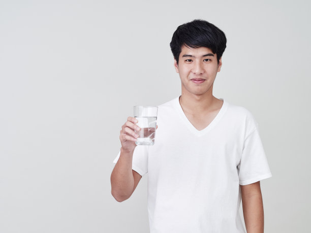 年轻的亚洲男人微笑着举着水杯在白色的背景。图片下载