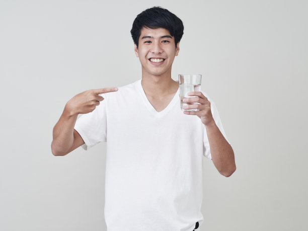 年轻的亚洲男人微笑着举着水杯在白色的背景。图片下载