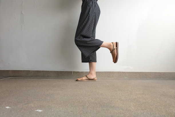 时髦的女人脚和腿上穿着金色的凉鞋和黑色的裤子在人行道地板上面。时尚、美观的设计理念。美丽的女性站在街道道路的背景。图片下载