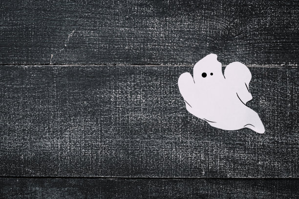 黑色的木头背景上的白色鬼魂服装。简约的万圣节的概念。牛皮纸鬼魂图片下载