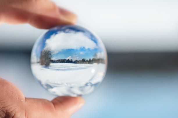 手指拿一个水晶或玻璃球，冬季景观反射，雪和树与蓝天，copyspace图片下载